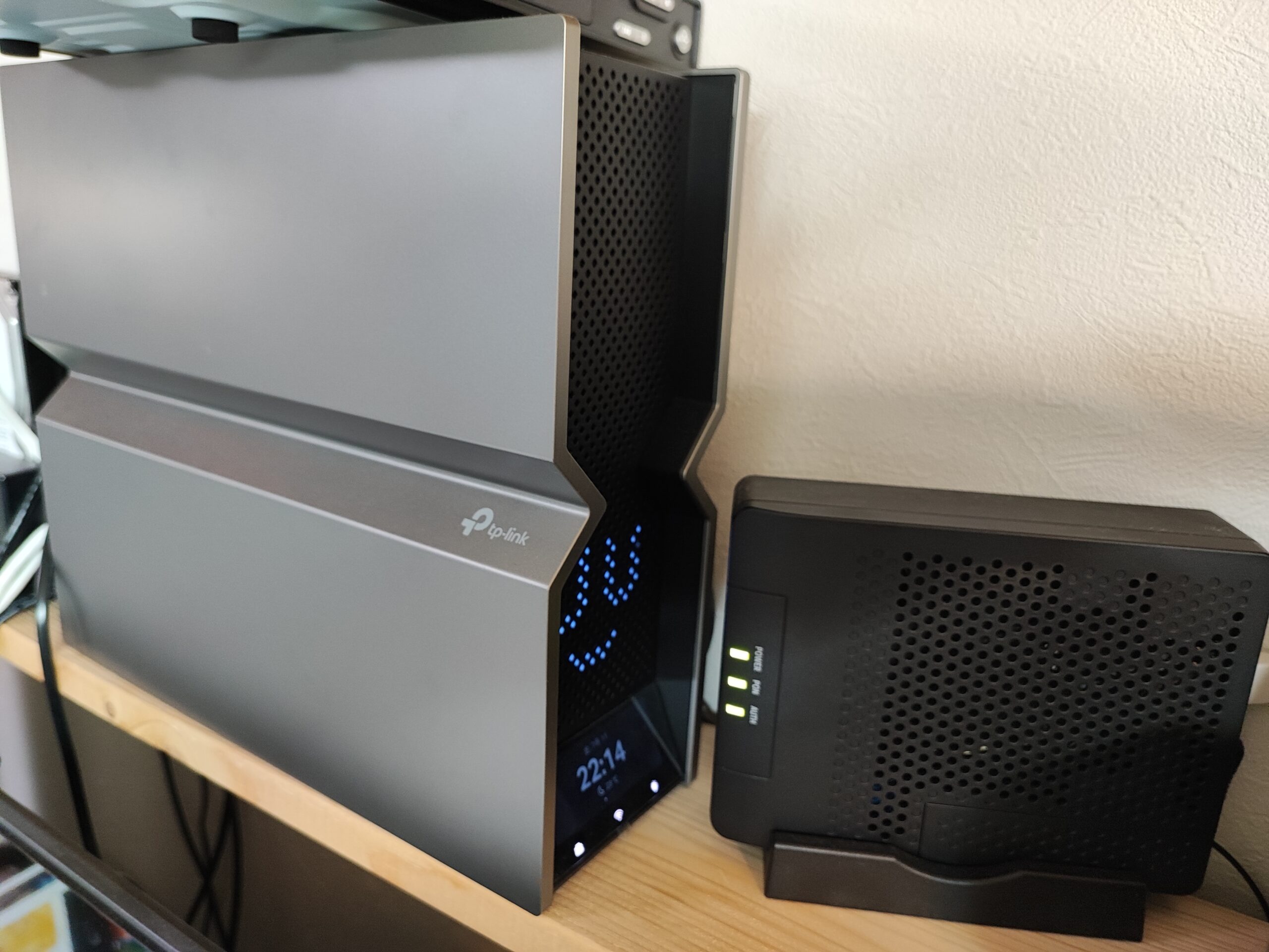 TP-Link BE900ルーターと光回線のONUが木製ラックに設置されている。