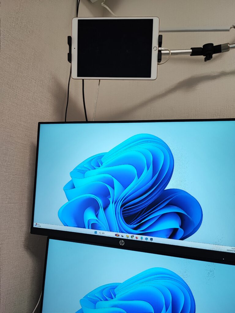壁面マウントされたiPadと、縦向きで配置されたデュアルディスプレイにWindows 11が表示されているデスク環境。