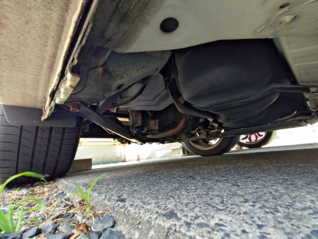 車両の下部を下から撮影した写真。オイルパン、排気管、サスペンション部品、車体のフレームが見える。