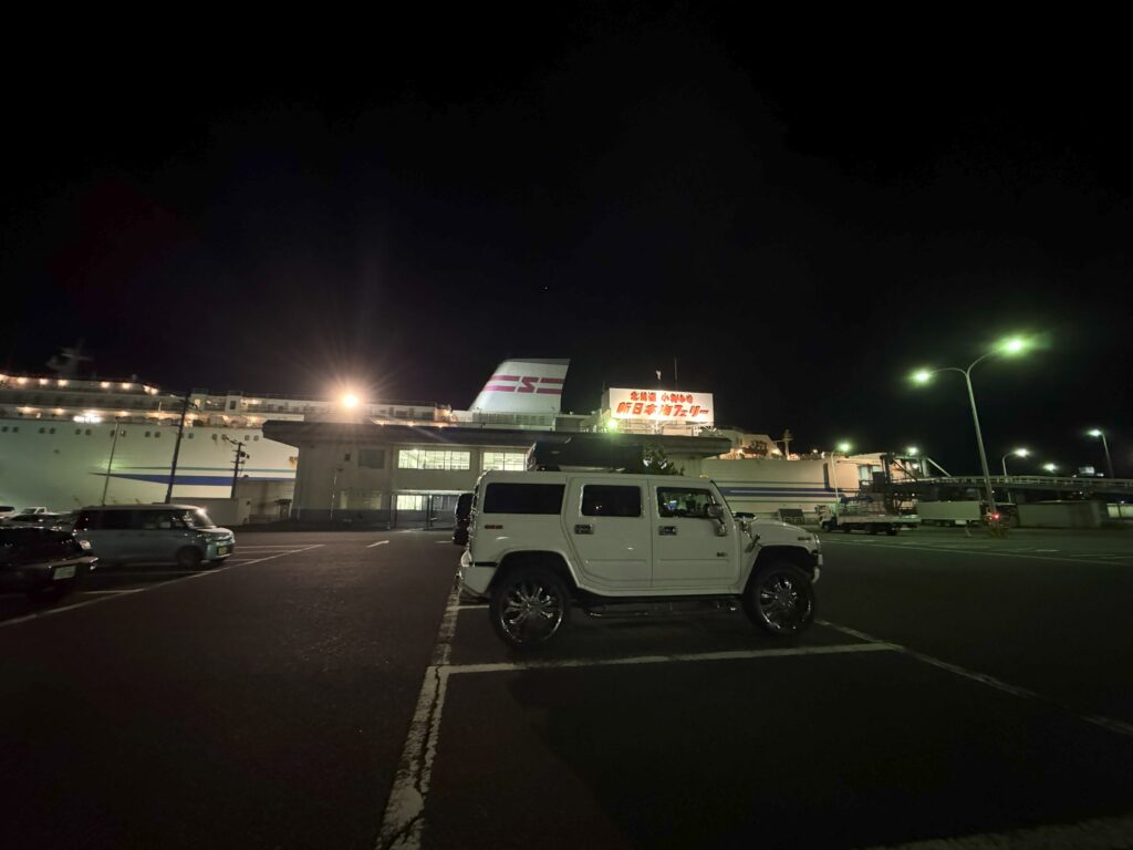 夜の新日本海フェリー乗り場に停車中の白いハマーH2とフェリーターミナルの風景。