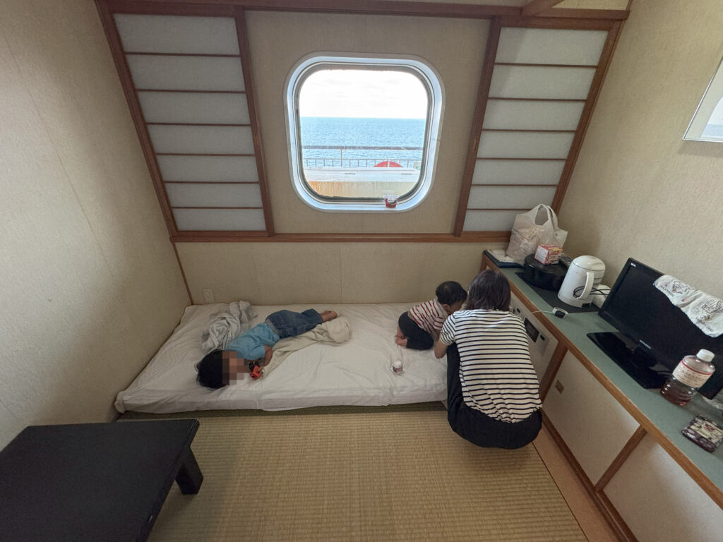 新日本海フェリーの和室個室でくつろぐ家族の様子。窓の外には広がる海が見える。