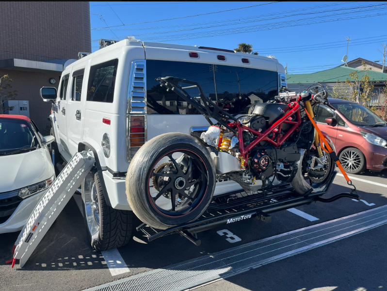 白いHUMMER H2のヒッチキャリアに積載された整備中の赤いドゥカティ製バイクとアルミ製ラダーレール