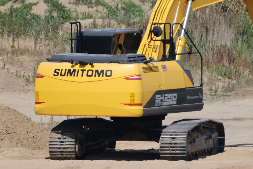建設現場の砂地に停車している黄色いSUMITOMO製油圧ショベル「SH250」の背面。