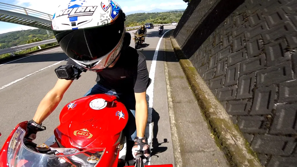 GoPro Hero Sessionをヘルメットに装着し、赤いバイクで走行するライダーのオンボード映像。背景には走行中の他のライダーも映っている。