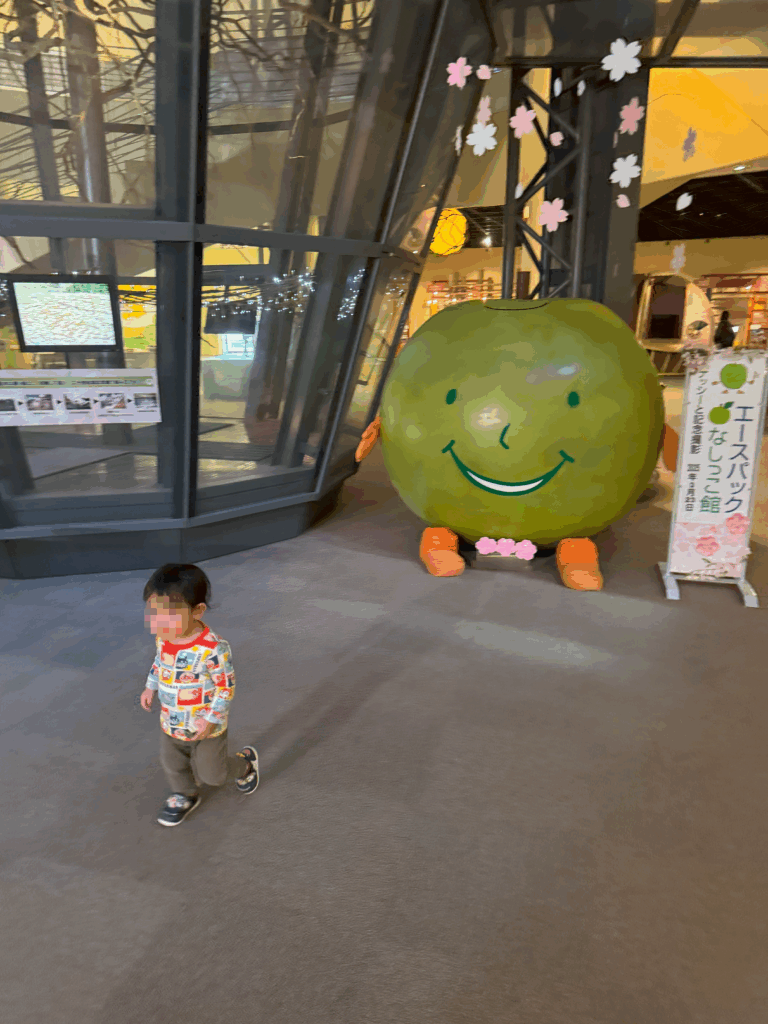 鳥取県倉吉市にある「エースパック なしっこ館」の入口前で撮影された写真。大きな梨のマスコットと一緒に子どもが写っている。
