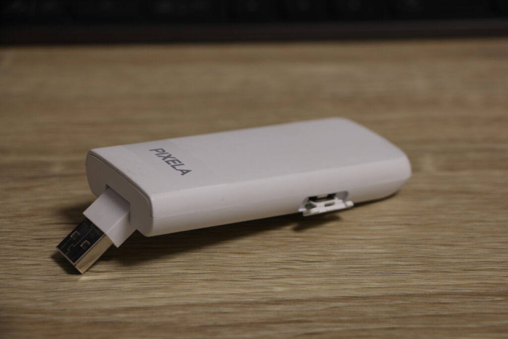 PIXELA製のUSB型モバイル回線アダプターがデスク上に置かれている。側面にはSIMカードスロットが見える