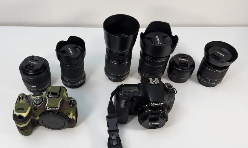 Canon EOS 60Dと複数のCanonレンズを並べた写真。手前には迷彩柄のカメラボディも見える。