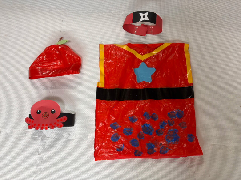 保育園の運動会で使用された手作り衣装。赤いビニール素材に黒帯と青い飾りが付けられ、手裏剣マークの頭飾りとセットになっている。タコの飾りがついた頭飾りとりんごの帽子は別の出し物で使用。