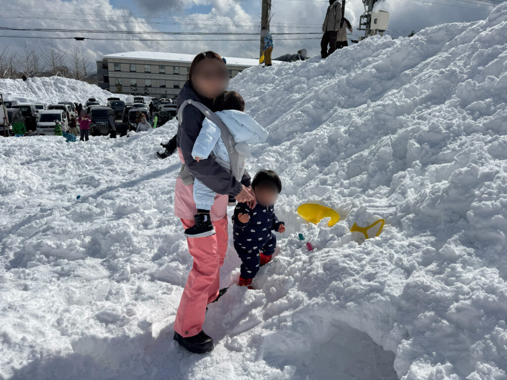 防寒着を着た親子が雪の斜面で雪遊びを楽しんでいる様子