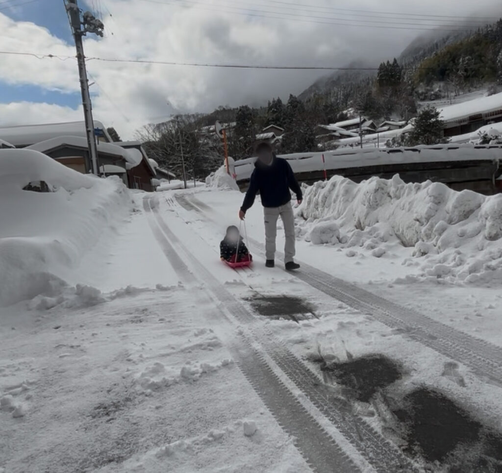 雪道をそりで滑る子どもを大人が引いて歩く冬の帰り道の様子