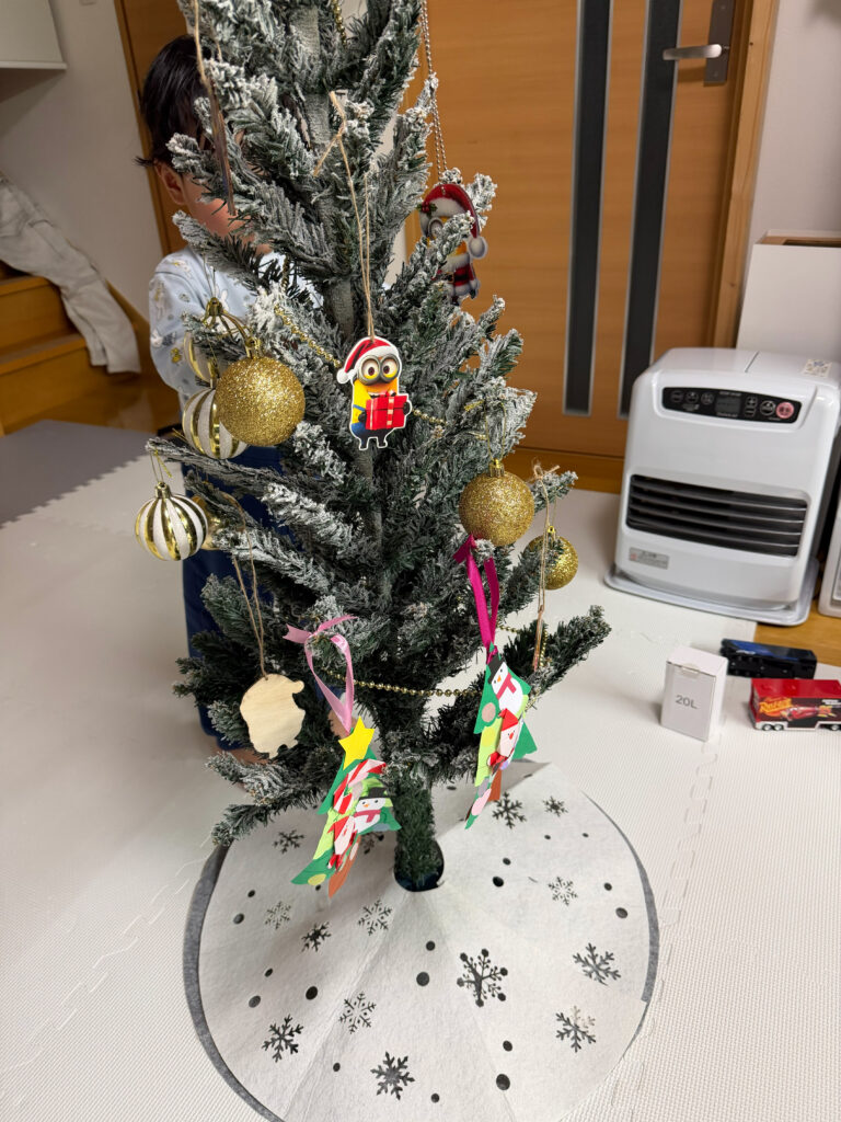 子どもが室内でクリスマスツリーに飾りつけをしている様子
