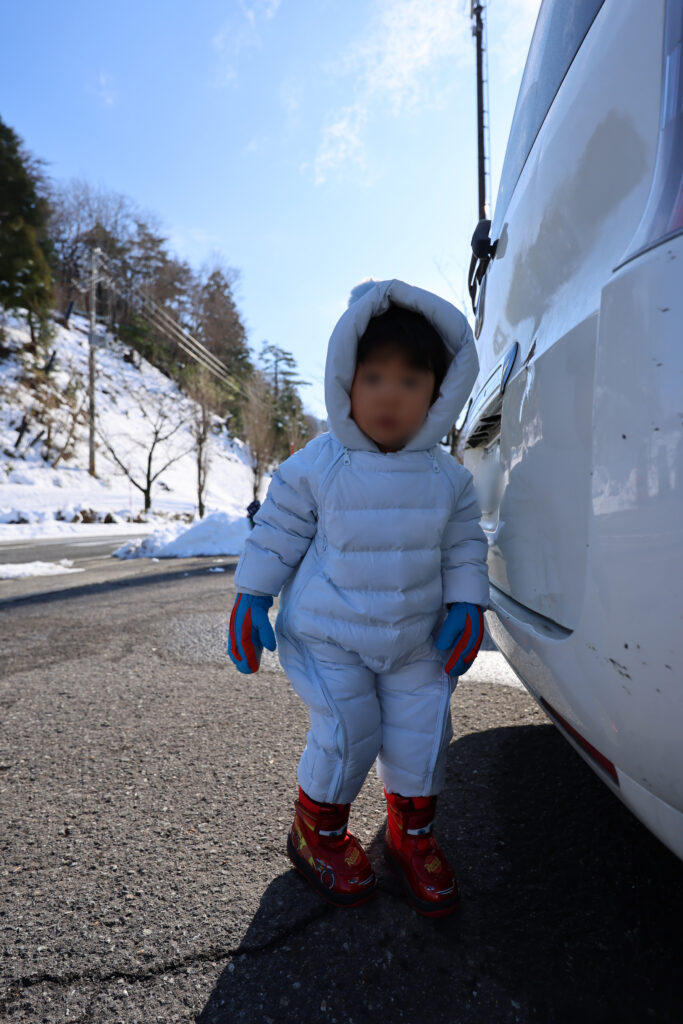 雪の日に防寒着を着た子どもが車の横に立って外出する準備をしている様子